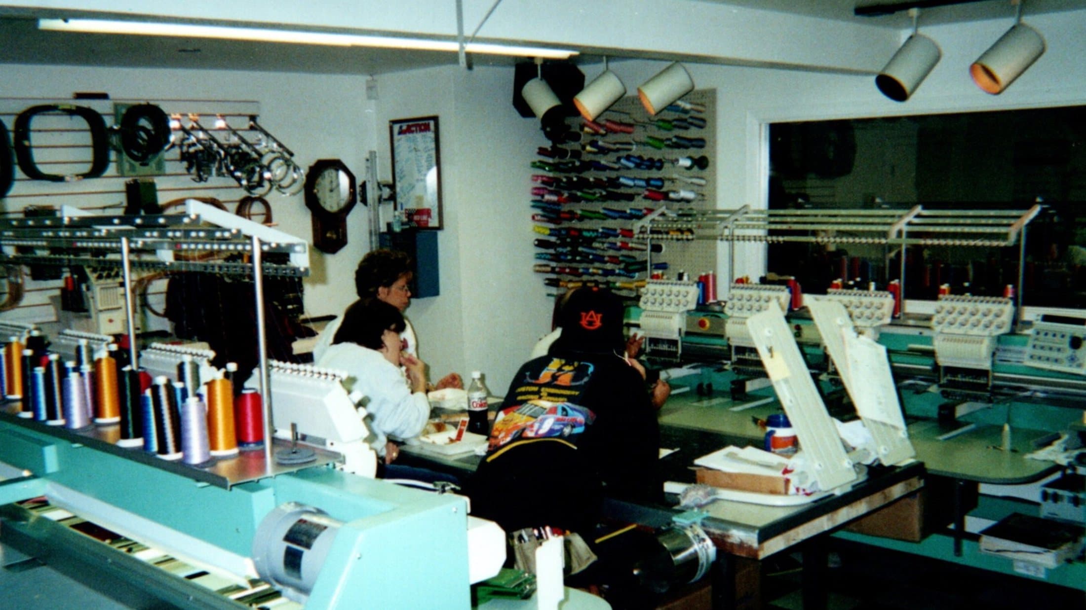 Dennis and Janet Davis at the original J&D Custom Embroidery shop in the 1990s — multi-head Tajima machines and a full thread color rack visible behind them
