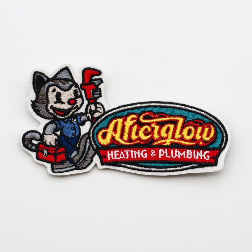 A custom embroidered patch for Afterglow Heating & Plumbing — a cartoon cat mascot holding a red pipe wrench beside a vintage script logo